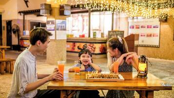 A family dining at a restaurant with a wooden table, string lights overhead, and a menu board in the background.