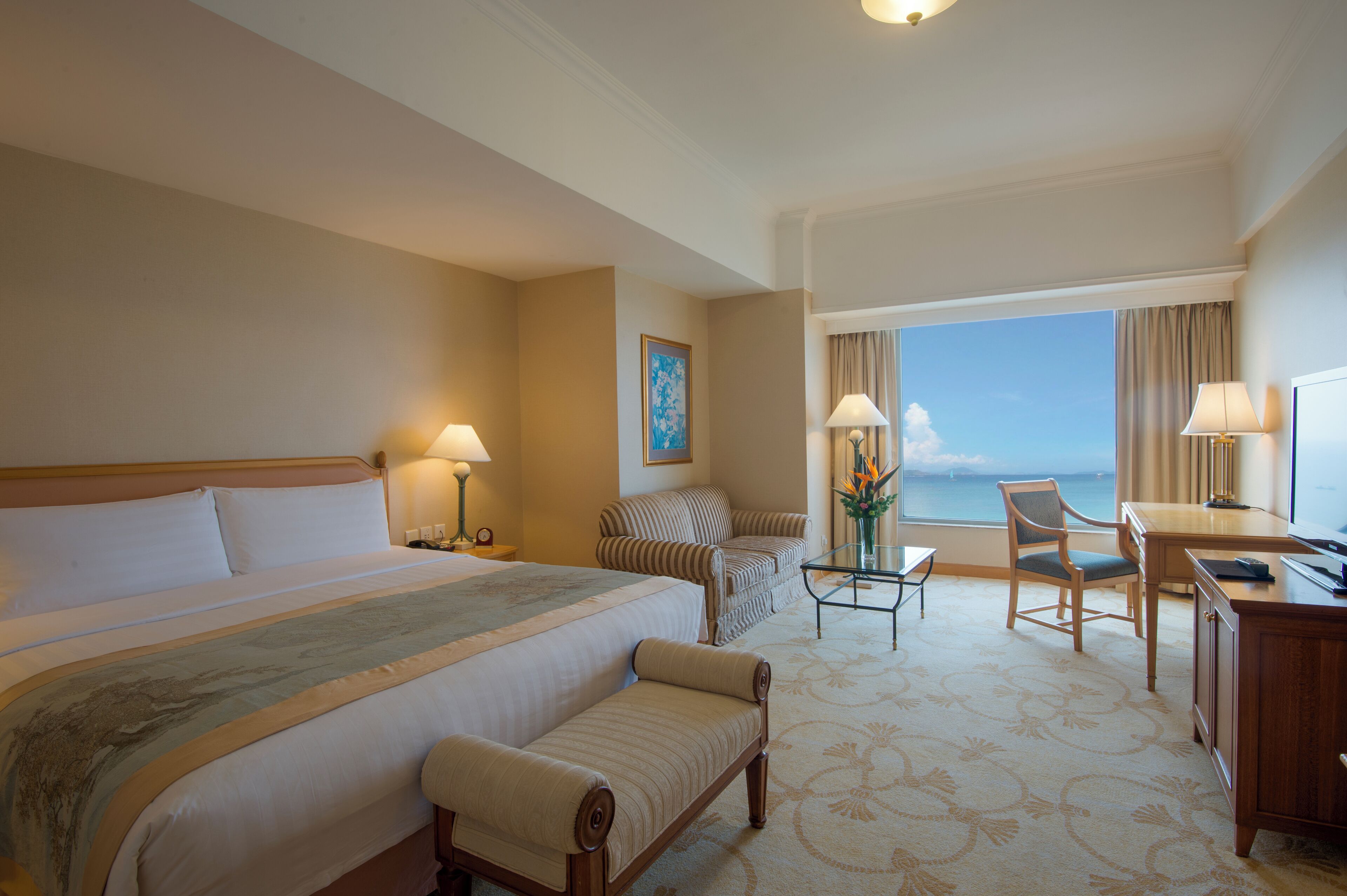 A hotel room with a large bed, a desk, a chair, and a view of the ocean.