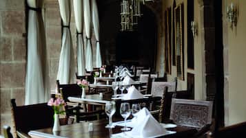 Un restaurant où les tables sont dressées pour le service, avec un mur en pierre et des luminaires suspendus.