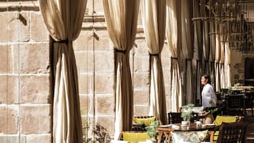An indoor dining area with tables and chairs, draped curtains, and hanging light fixtures.