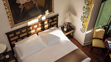 Habitación de hotel con una cama grande, una mesita de noche con lámpara, una pequeña mesa con un jarrón y una silla.