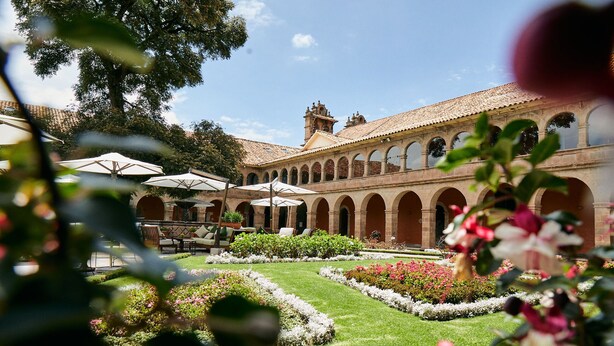 Un patio con un edificio que cuenta con paseos en arco y asientos al aire libre.