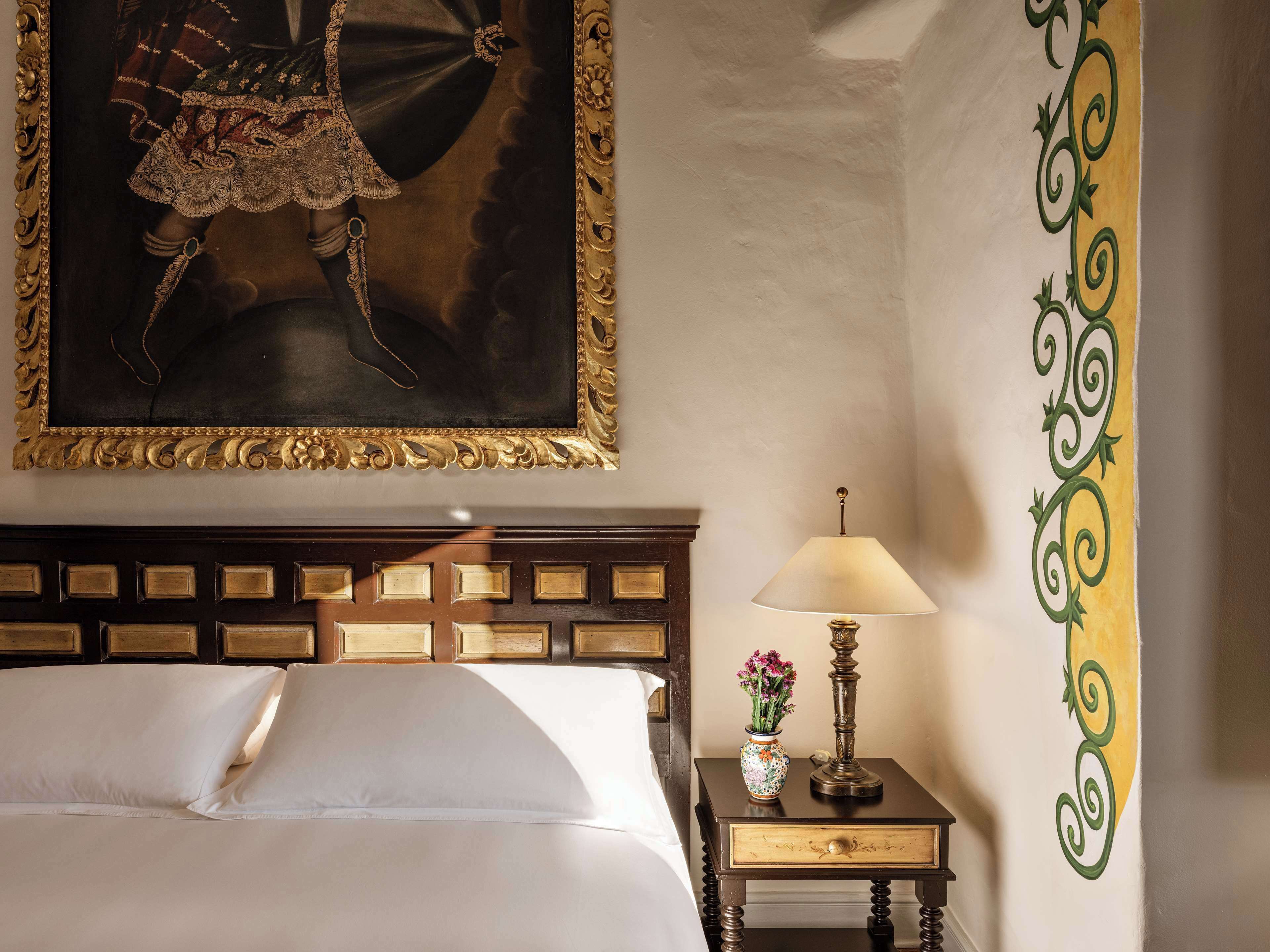 Een hotelkamer met een bed, een nachtkastje met een lamp en vaas, en een lijst met een schilderij aan de muur.