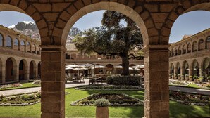 A courtyard with stone arches, a central tree, and a seating area with umbrellas. - Monasterio, A Belmond Hotel, Cusco (Cusco)