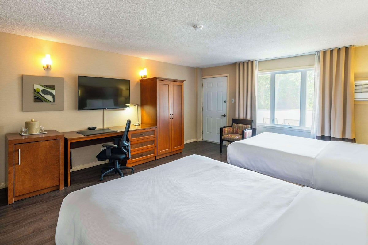 A hotel room with two beds, a desk with a chair, a wardrobe, a television, and a window with curtains.