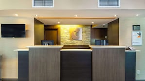 A reception desk with a stone wall backdrop, a mounted television, and a framed certificate on the wall. - Comfort Inn Mont Laurier (Mont-Laurier)