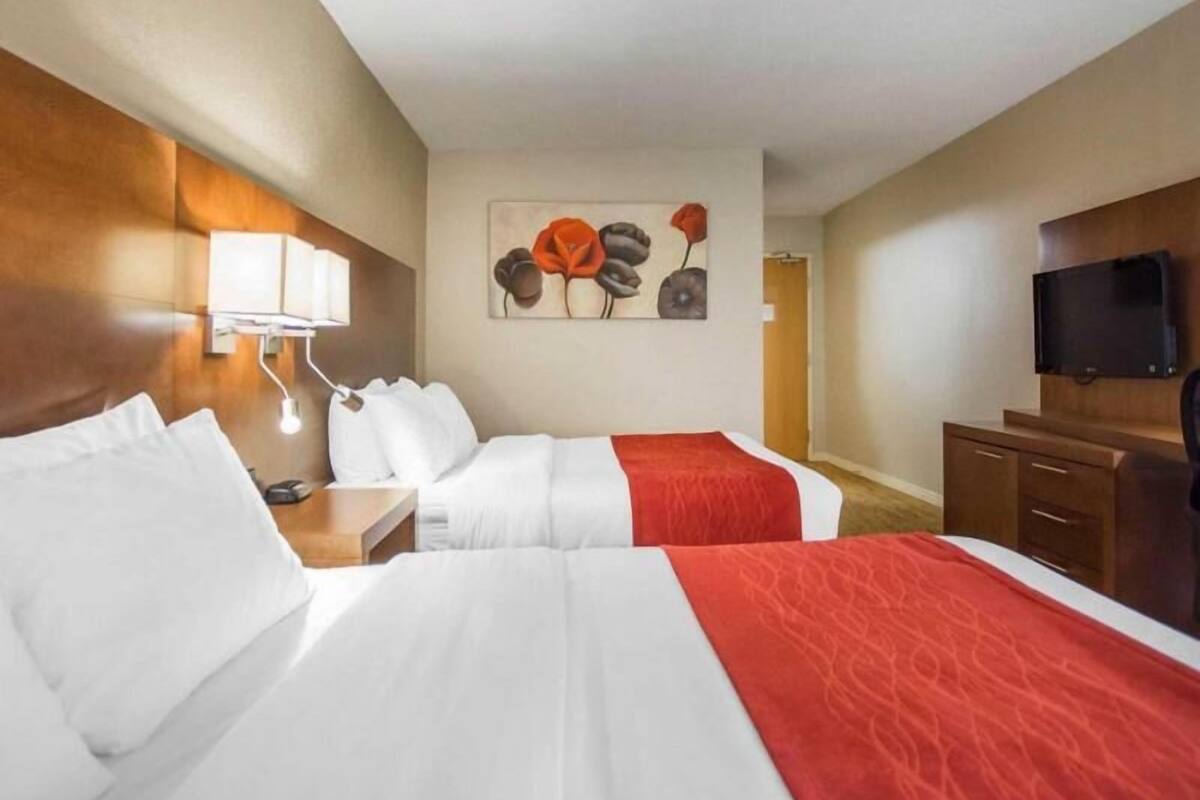 A hotel room with two beds, a flat-screen TV, a painting on the wall, and a wooden headboard.