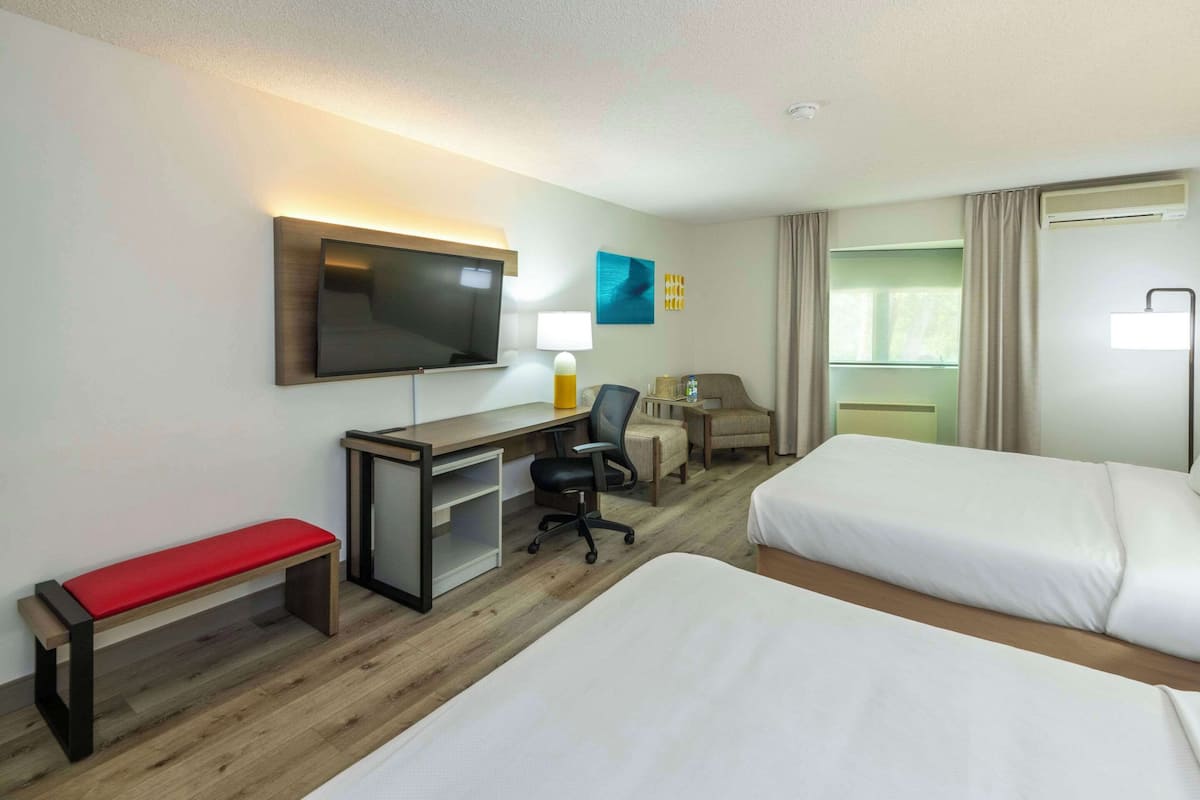 A hotel room with two beds, a desk with a chair, a TV, and a window with curtains.