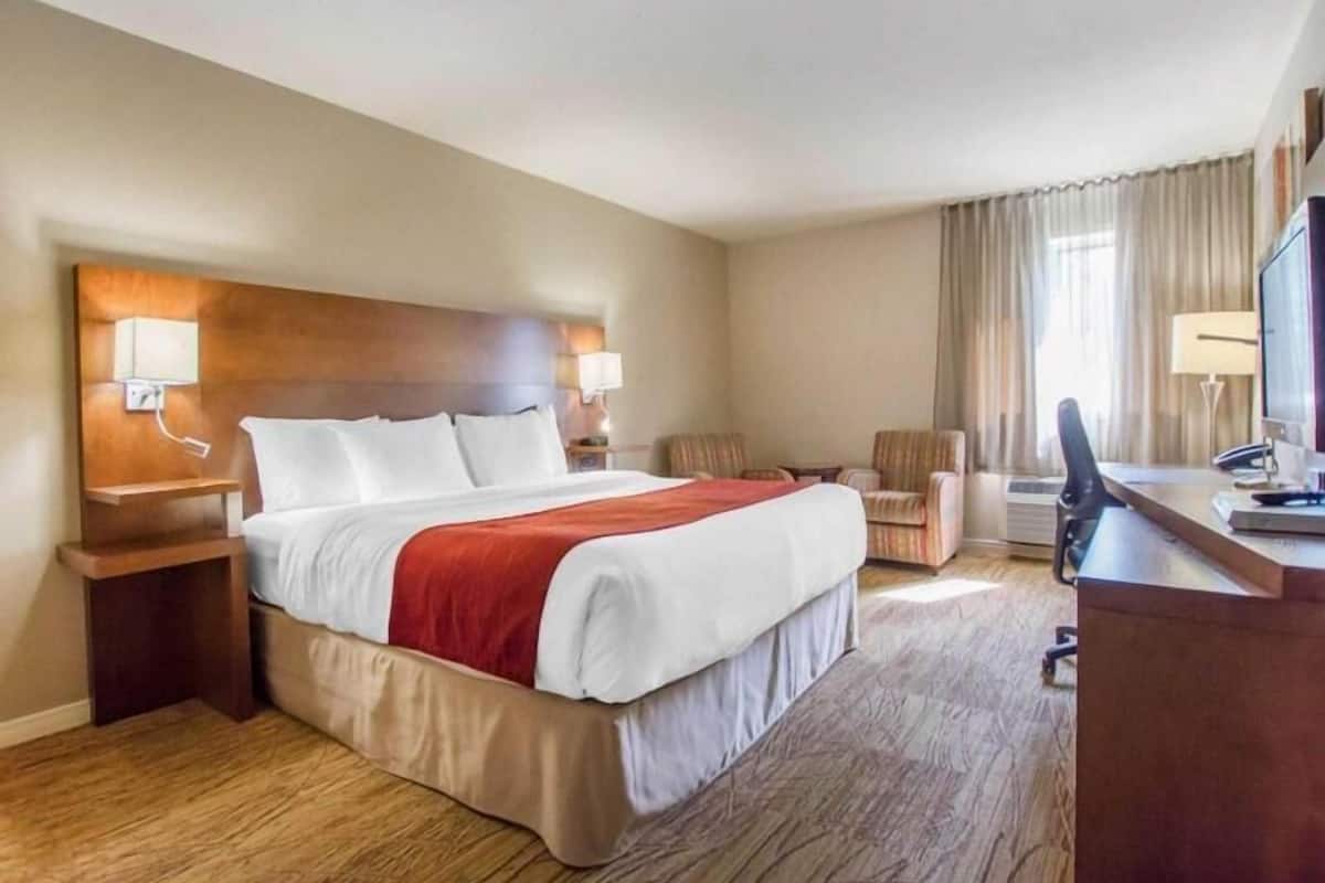 A hotel room with a large bed, a desk with a computer, a chair, and a TV.