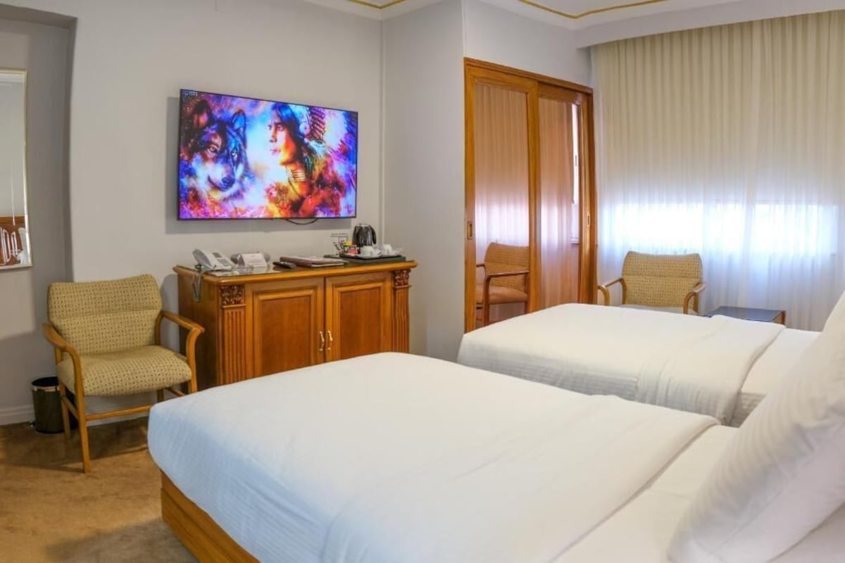 Camera d'albergo con due letti, un armadietto in legno con un telefono, una sedia e una TV appesa al muro.