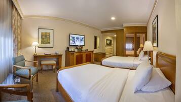 A hotel room with two beds, a desk, a chair, and a TV.