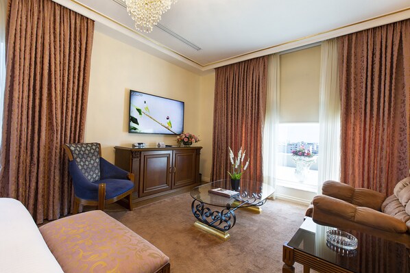 A hotel room with a large flat-screen TV, a sofa, a chair, a coffee table, and a carpeted floor. - Amman International (Amman)