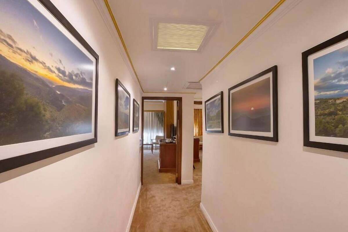 A hallway with framed landscape paintings on the walls, leading to a room with a desk and chair.