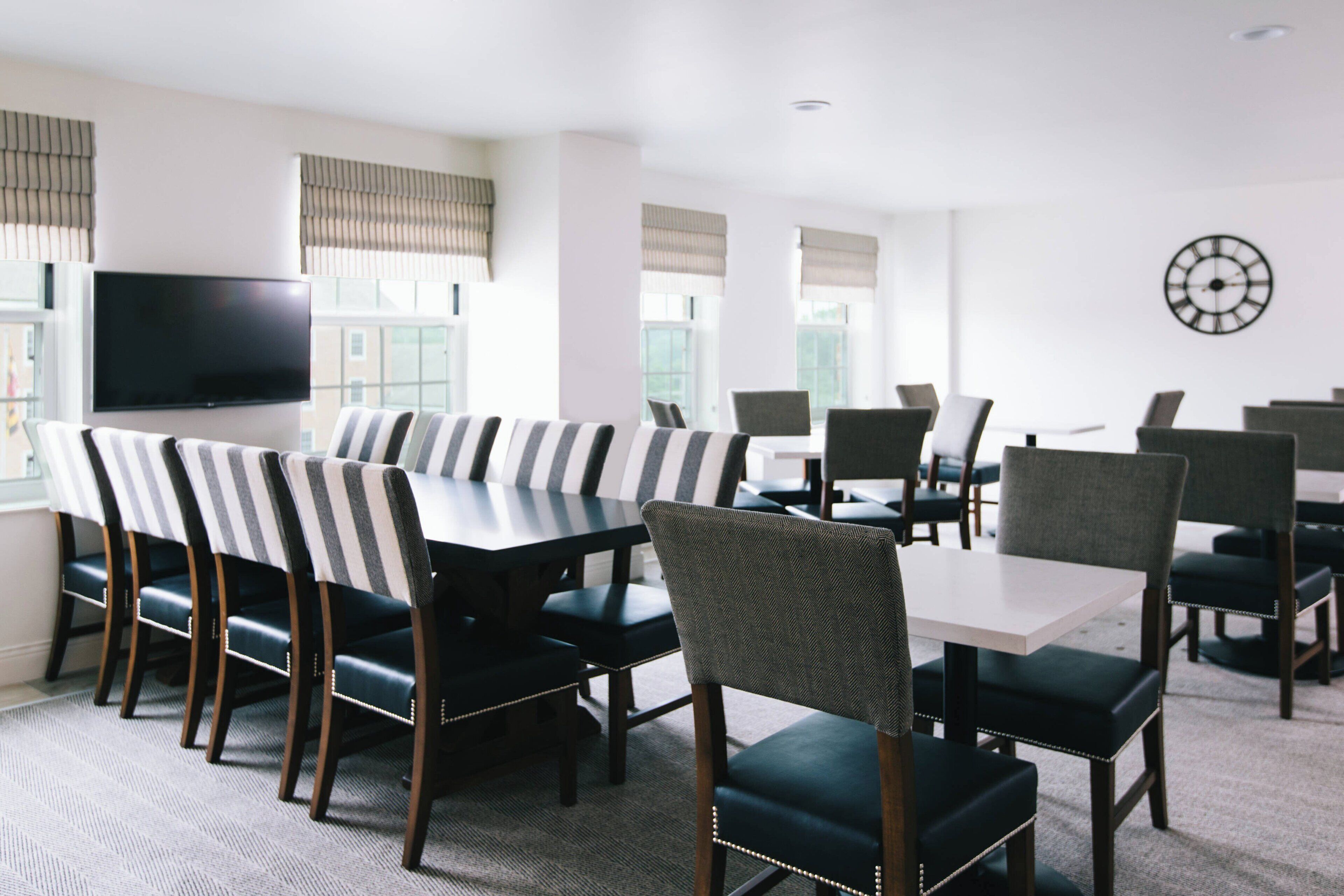 A conference room with a large table, chairs, a flat-screen TV, and windows with blinds.