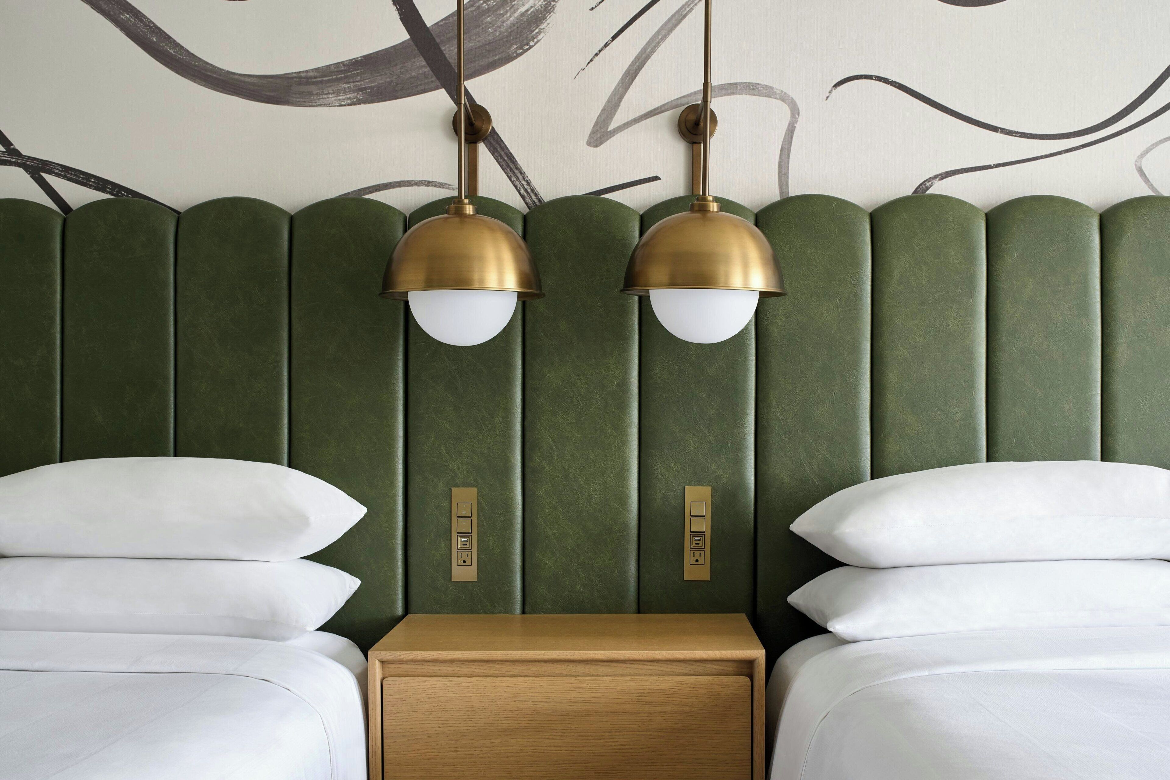 A hotel room with a green upholstered headboard, two bedside tables, and two lamps.