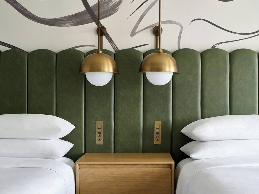 A hotel room with a green upholstered headboard, two bedside tables, and two lamps.