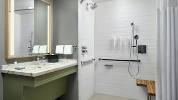 A modern bathroom with a marble sink, a large mirror, a shower with a handheld showerhead, and a wooden bench.