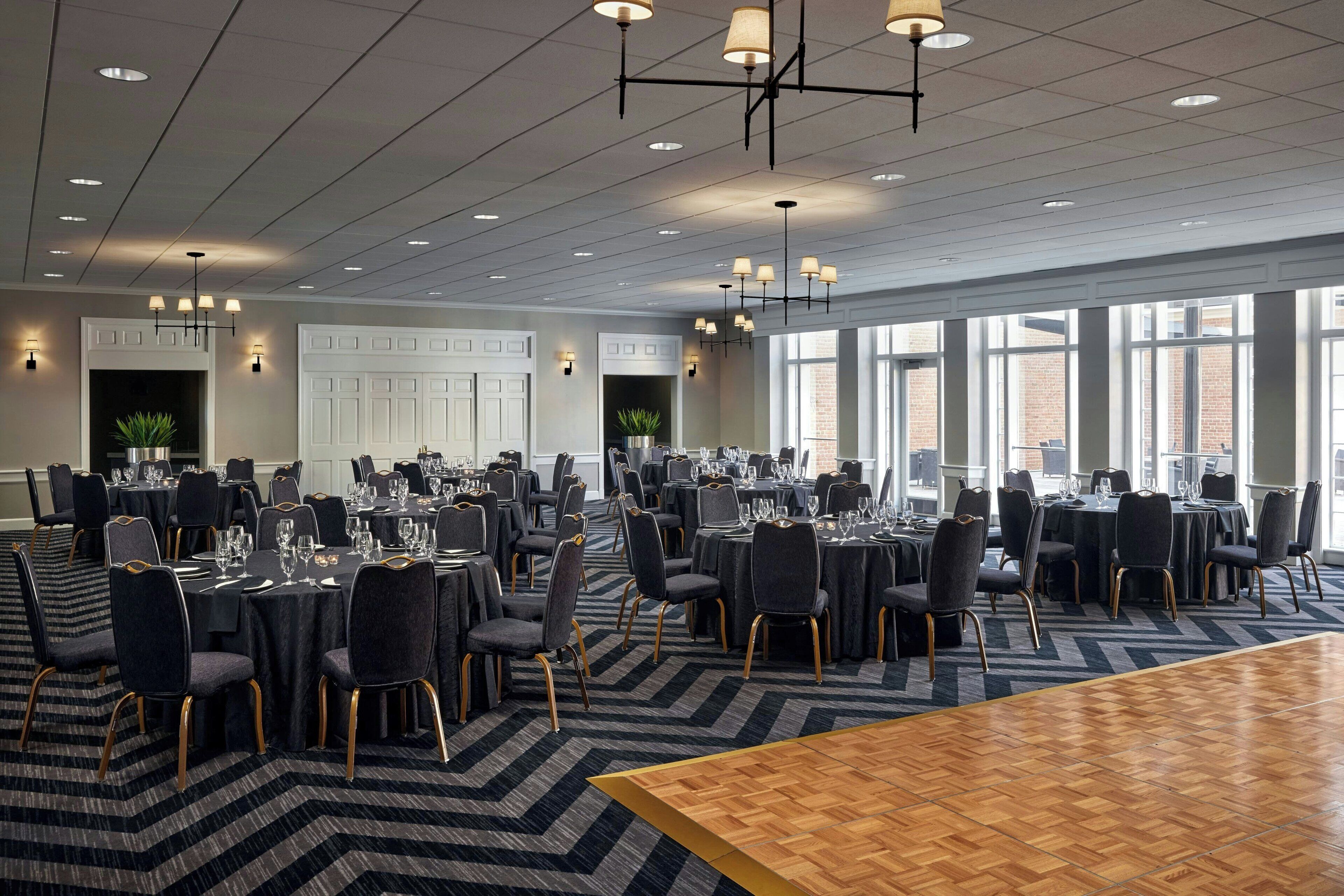 A large banquet hall with multiple round tables set for dining, arranged in rows with chairs.