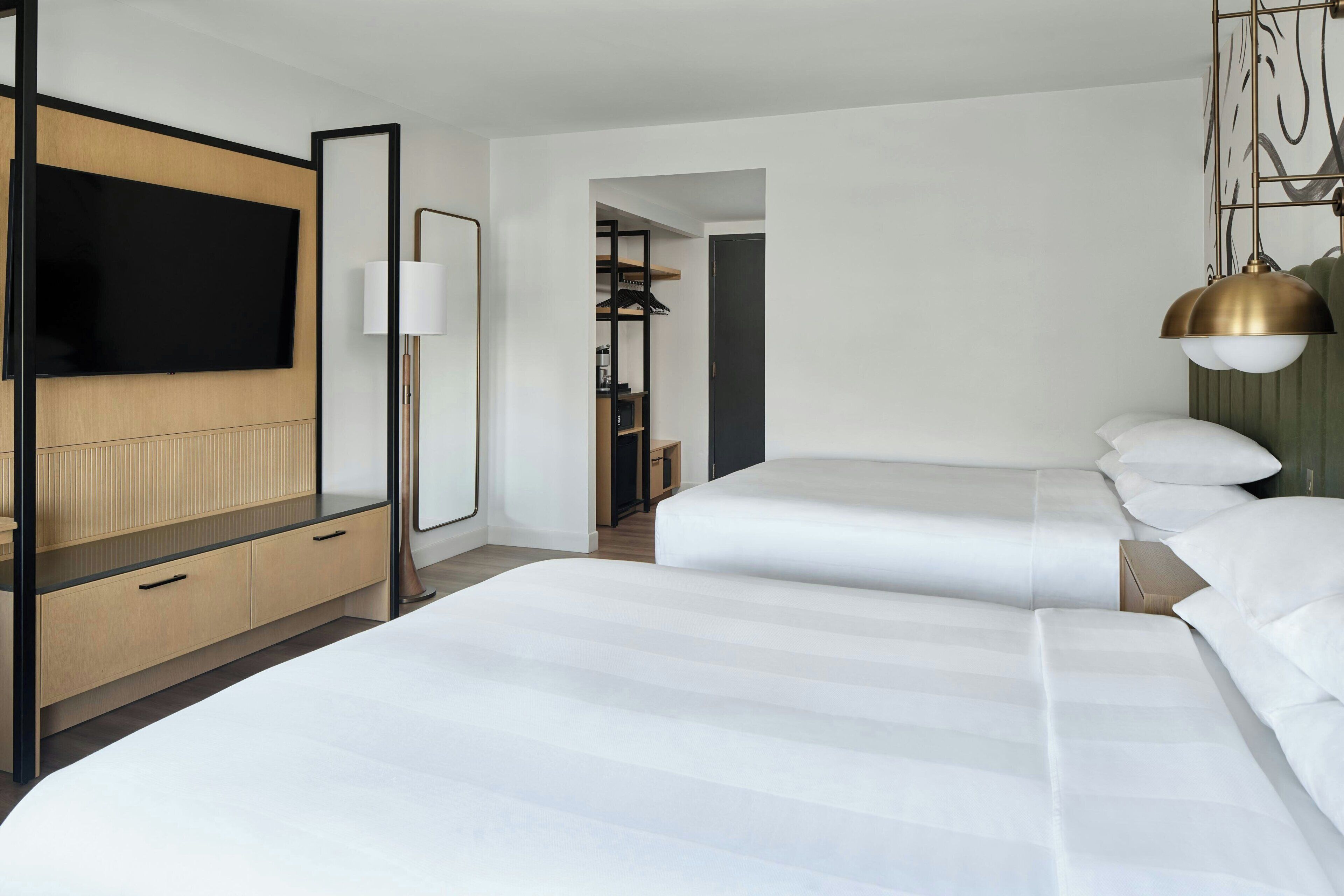 A hotel room with a large bed, a TV, a desk with drawers, a lamp, and a wardrobe.