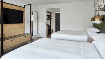 A hotel room with a large bed, a TV, a desk with drawers, a lamp, and a wardrobe.
