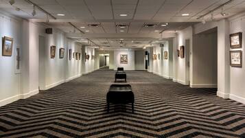 A long hallway with a patterned carpet, framed pictures on the walls, and a bench in the center.