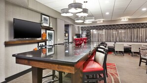 A modern dining area with a large rectangular table, red upholstered chairs, and a flat-screen TV mounted on the wall. - Hampton Inn Columbus/Delaware I-71 North (Sunbury)