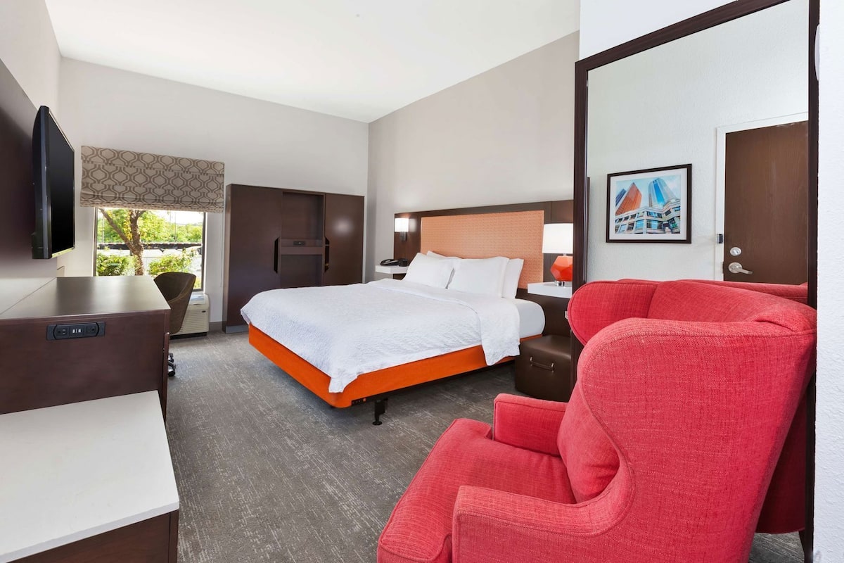A hotel room with a bed, a desk, a chair, a TV, and a window with a view.