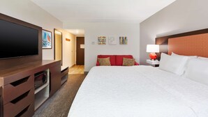 A hotel room with a large bed, a flat-screen TV, a wooden dresser, and a red sofa. - Hampton Inn Columbus/Delaware I-71 North (Sunbury)
