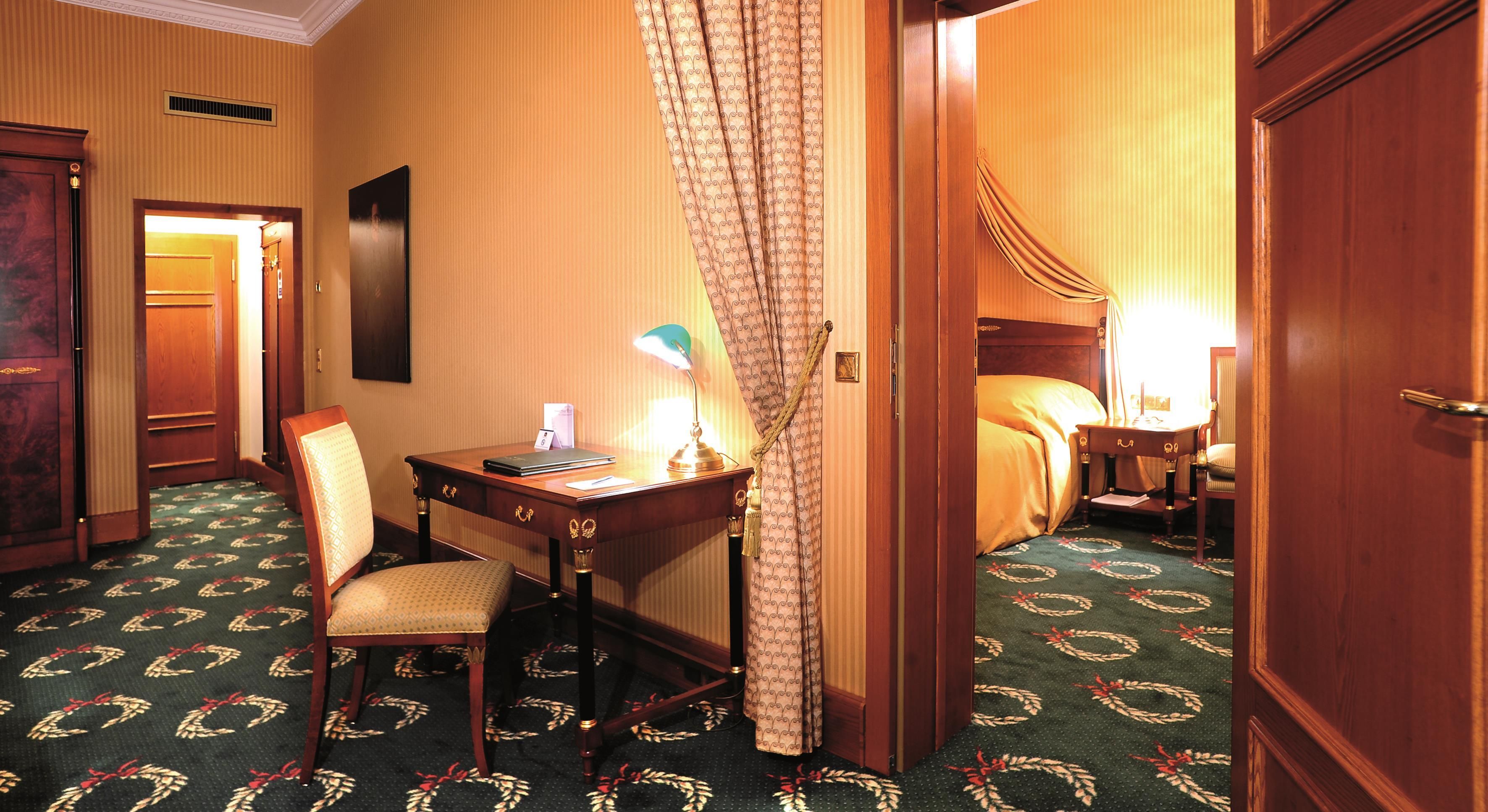 Une chambre d’hôtel équipée d’un bureau, d’une chaise, d’un lit et d’une grande fenêtre avec des rideaux.
