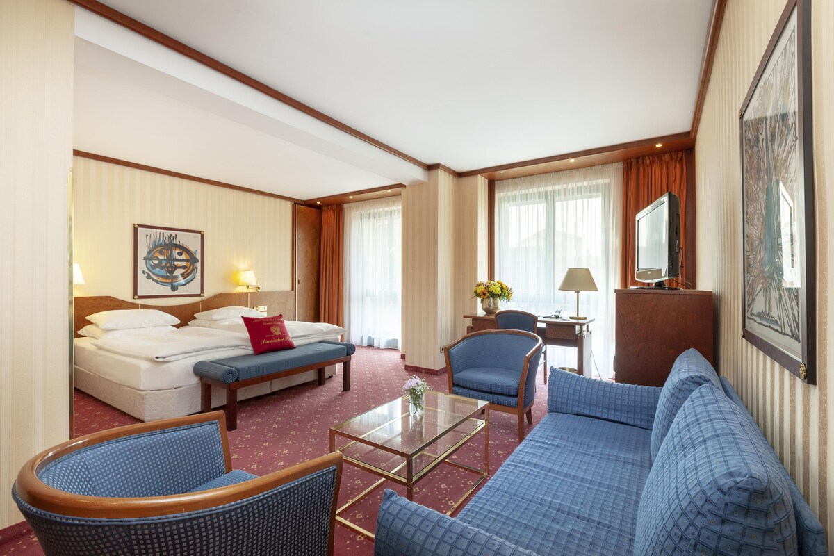Une chambre d’hôtel comprenant un lit, deux fauteuils, un canapé, un bureau avec une lampe et un téléviseur.