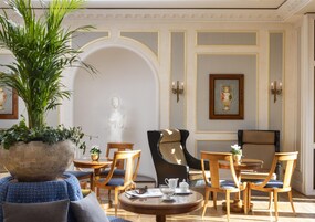 Una habitación bien iluminada con una planta grande en maceta, un busto y un comedor con sillas y una mesa.
