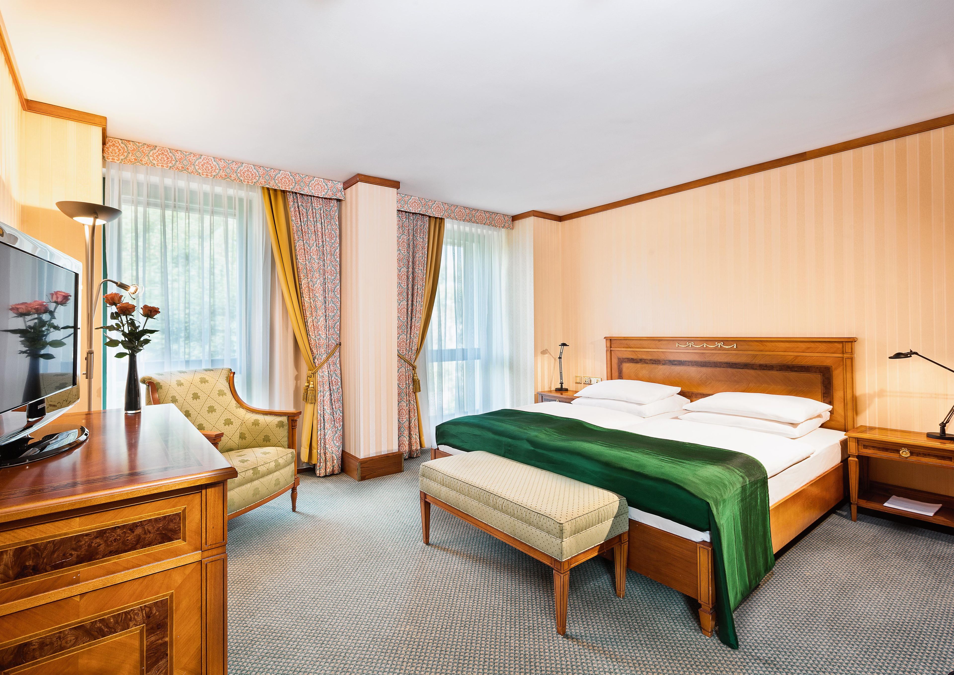 A hotel room with a bed, a desk, a chair, a TV, and a window with curtains.