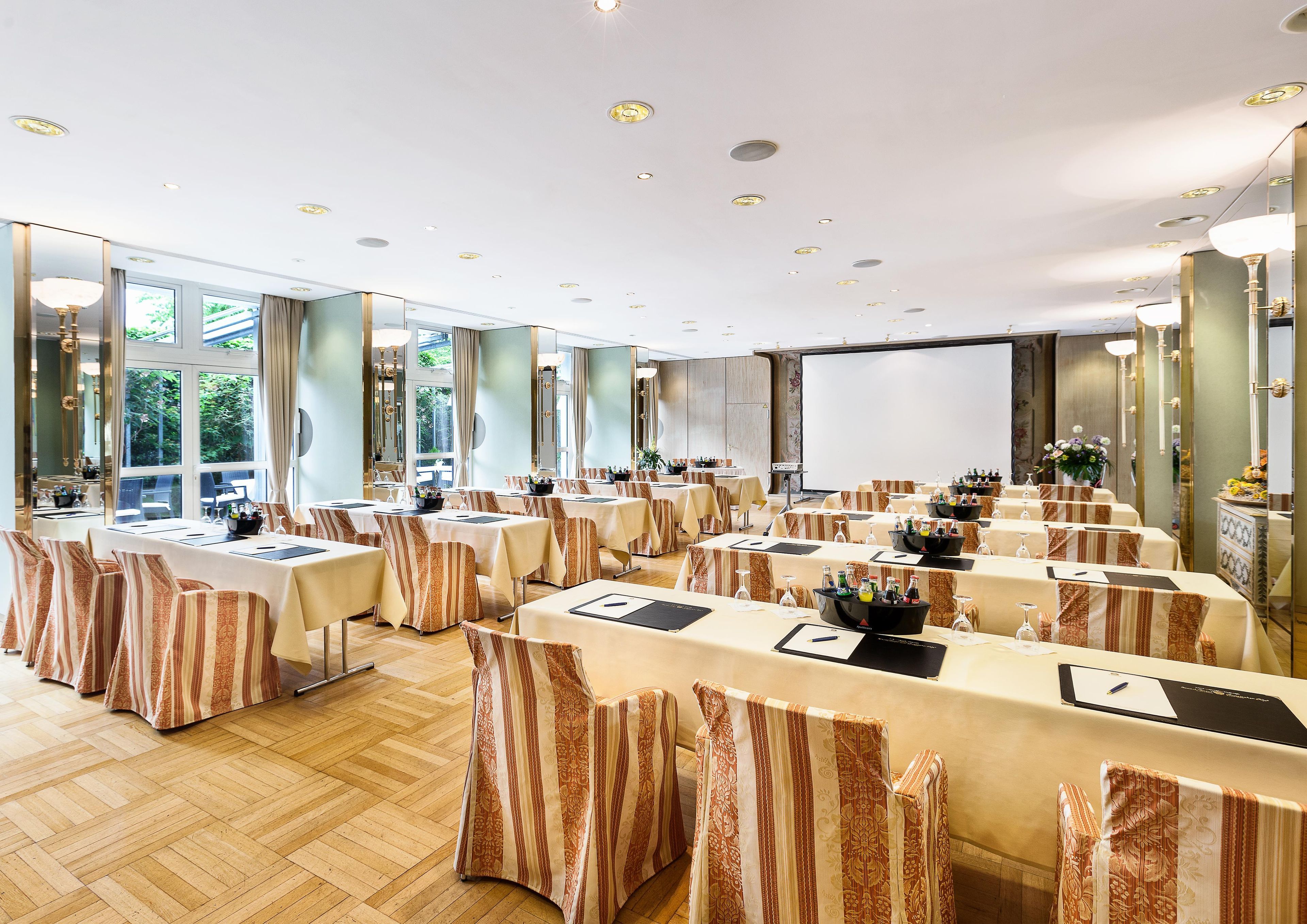 A conference room with tables set for a meeting, large windows, and a projector screen.