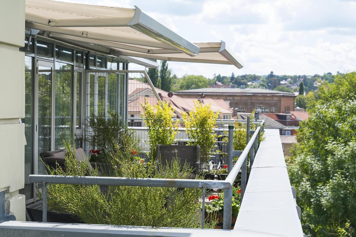 A balcony with a glass enclosure, metal railing, and a view of buildings and trees.