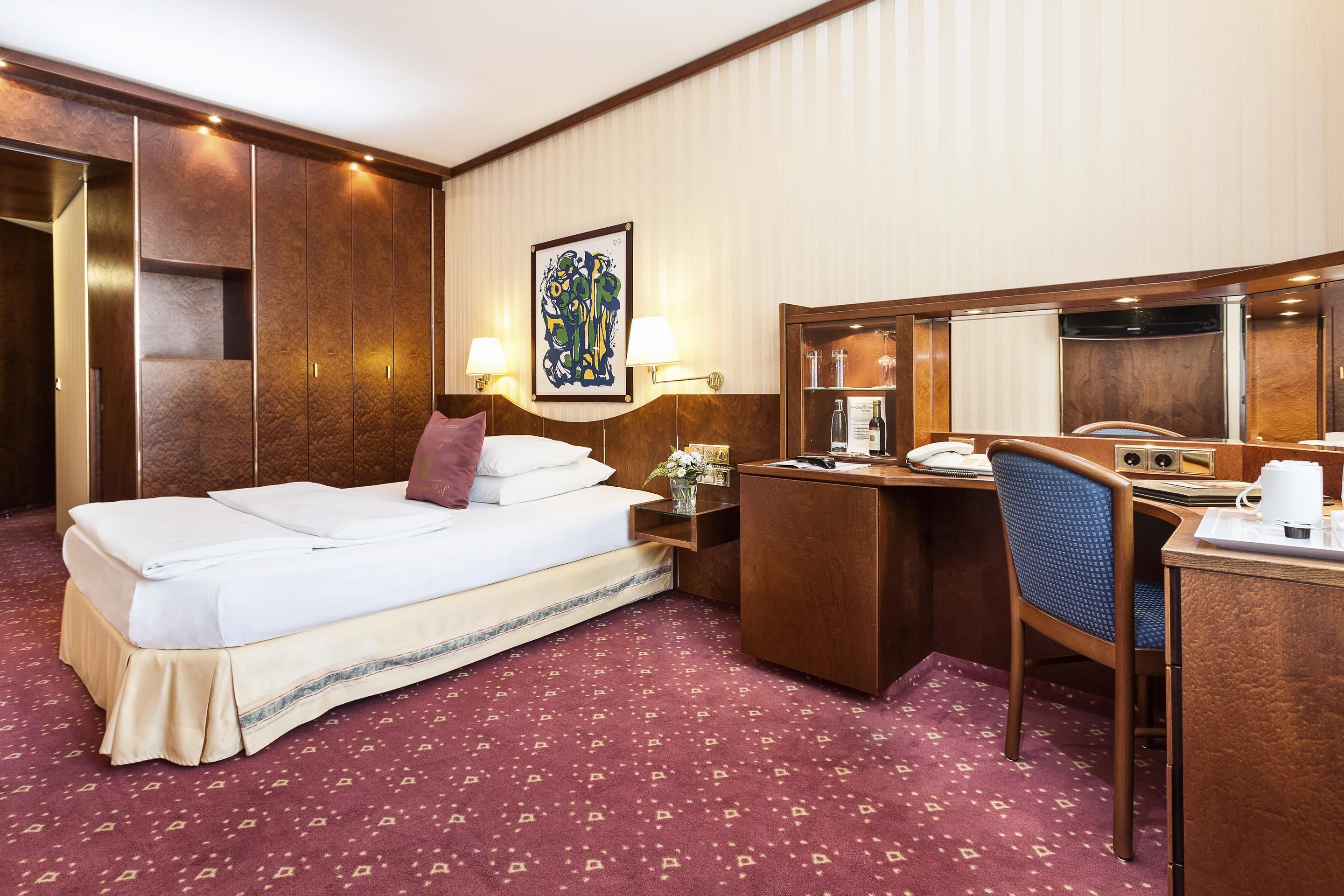 A hotel room with a bed, desk, chair, and a large mirror.