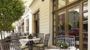 An outdoor café with tables and chairs, a tree, and a building with large windows. - Best Western Premier Grand Hotel Russischer Hof (Weimar)