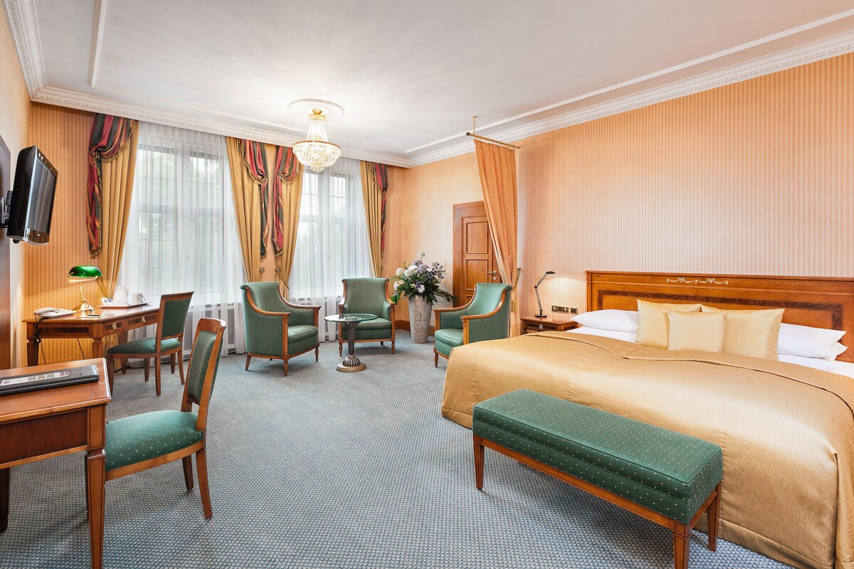 Une chambre d’hôtel avec un grand lit, deux fauteuils, un bureau avec une lampe et un téléviseur.