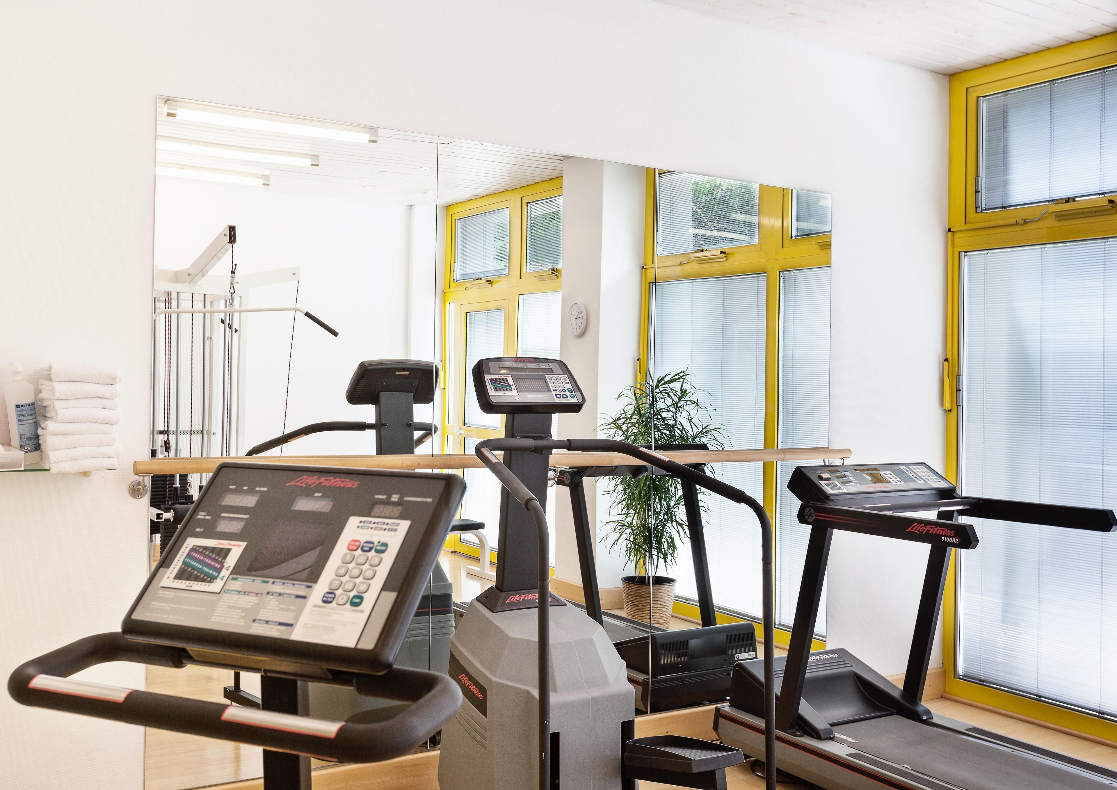 A gym with exercise equipment, a mirror, and a window with blinds.