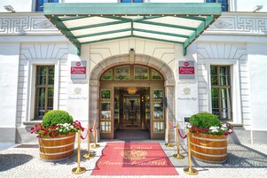 La entrada de un hotel con un arco imponente, una alfombra roja y dos macetas grandes.