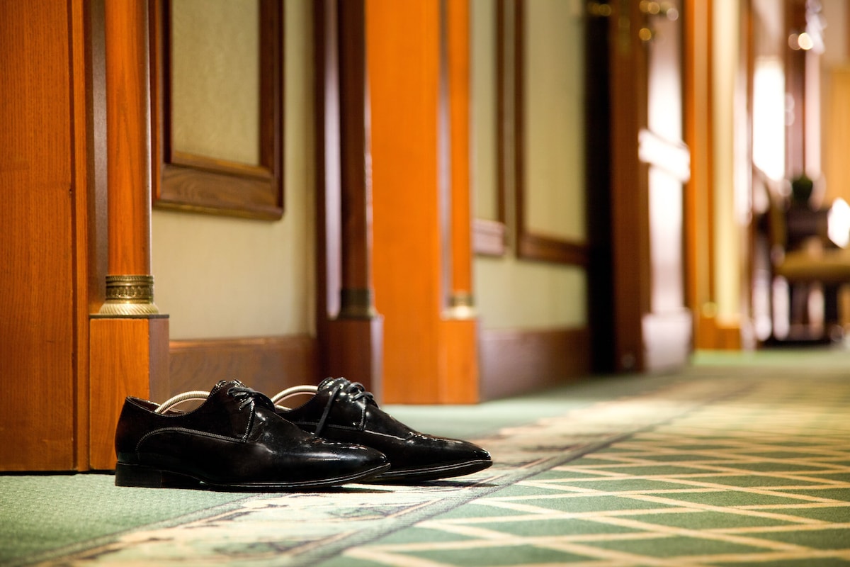 A pair of shoes on a patterned carpet in a hallway with wooden doors and a green carpet.