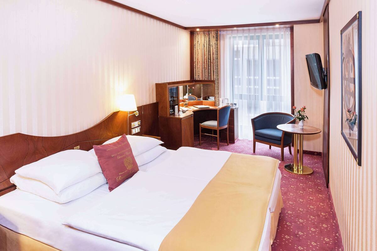 A hotel room with a large bed, a desk, a chair, and a small table.