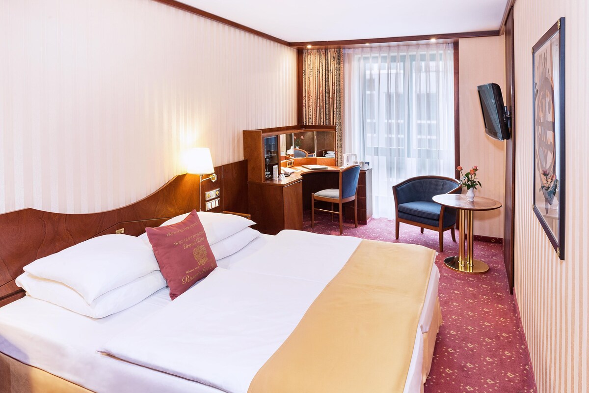 Une chambre d’hôtel avec un grand lit, un bureau, une chaise, une petite table et un téléviseur.