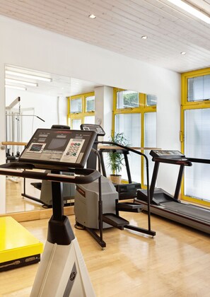 A gym with exercise equipment, including treadmills and a stationary bike, and large windows with yellow frames.