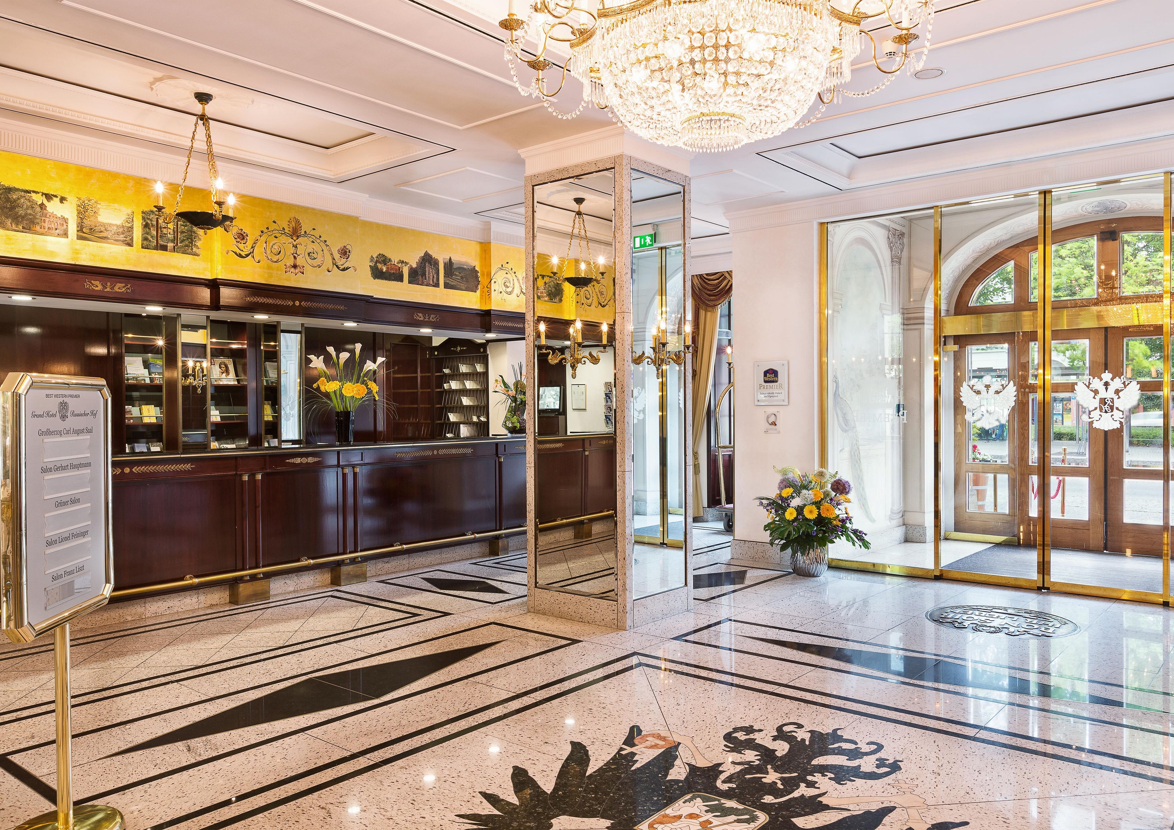 Un vestíbulo de hotel con una recepción, una araña y un espejo grande.