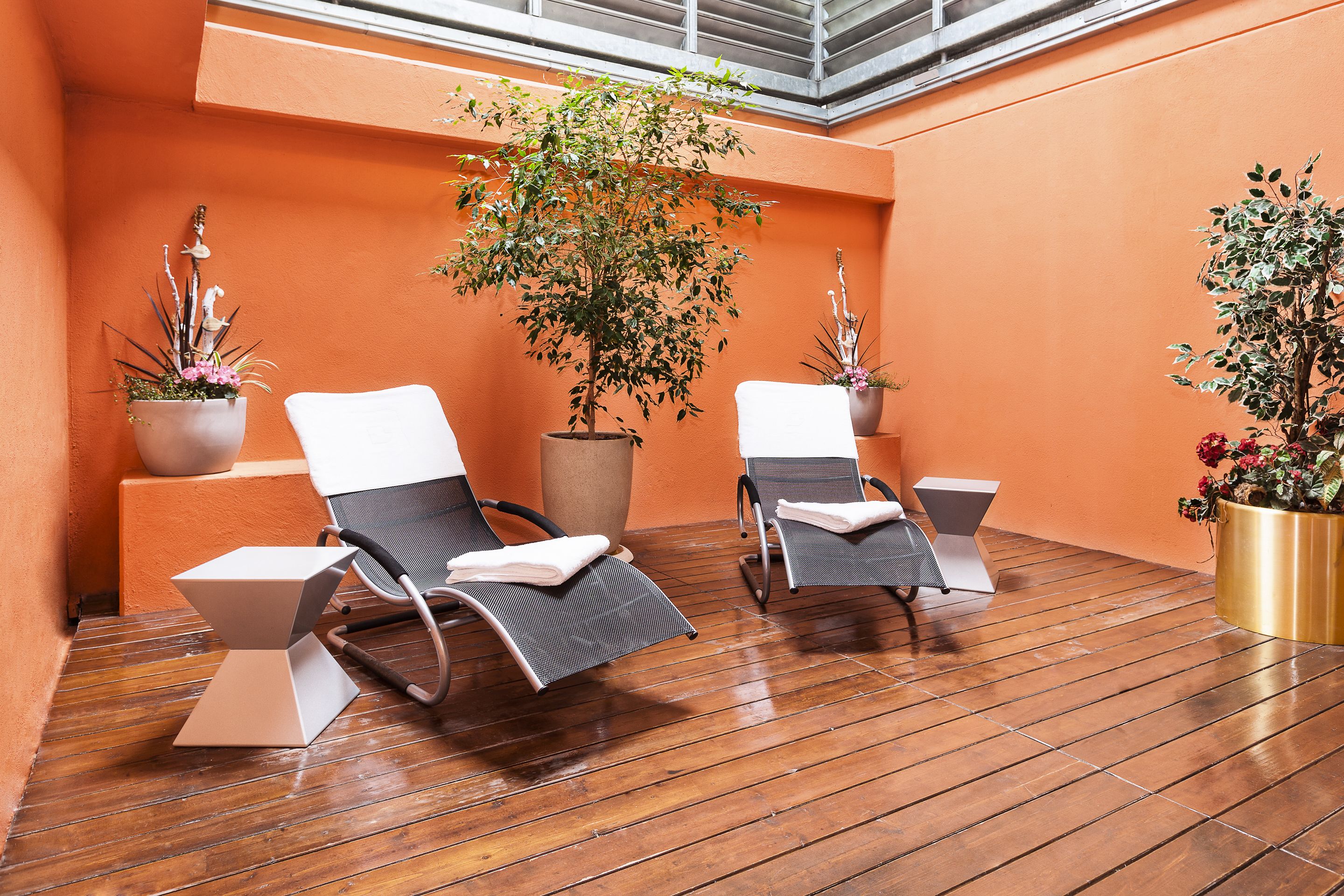 A sunlit outdoor seating area with two lounge chairs and potted plants.