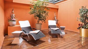 A sunlit outdoor seating area with two lounge chairs and potted plants.