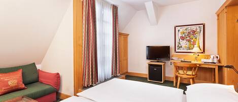 A hotel room with a bed, a desk with a computer, a television, and a window with curtains.