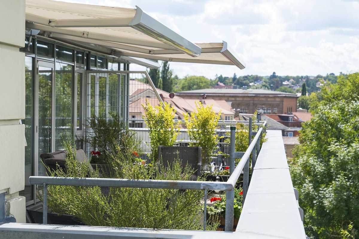 A balcony with a glass enclosure, metal railing, and a view of buildings and trees.