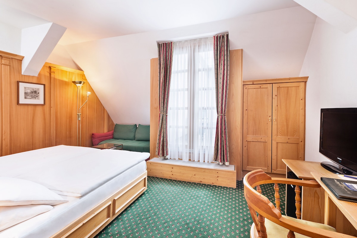 A room with a bed, a desk, a chair, a television, a window with curtains, and a wardrobe.