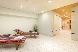A clean, modern waiting area with two lounge chairs, a potted plant, and a tiled floor.